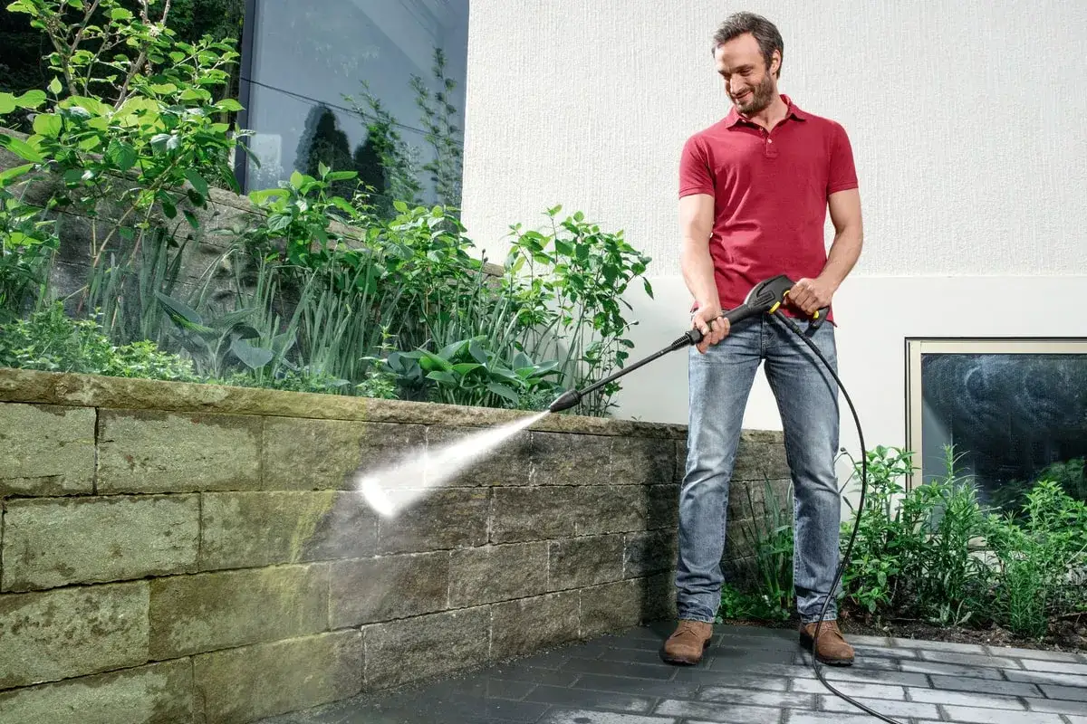 Mężczyzna myje kamienny murek myjką Karcher. Dowiedz się, dlaczego zostają smugi po myjce Karcher i jak ich unikać.