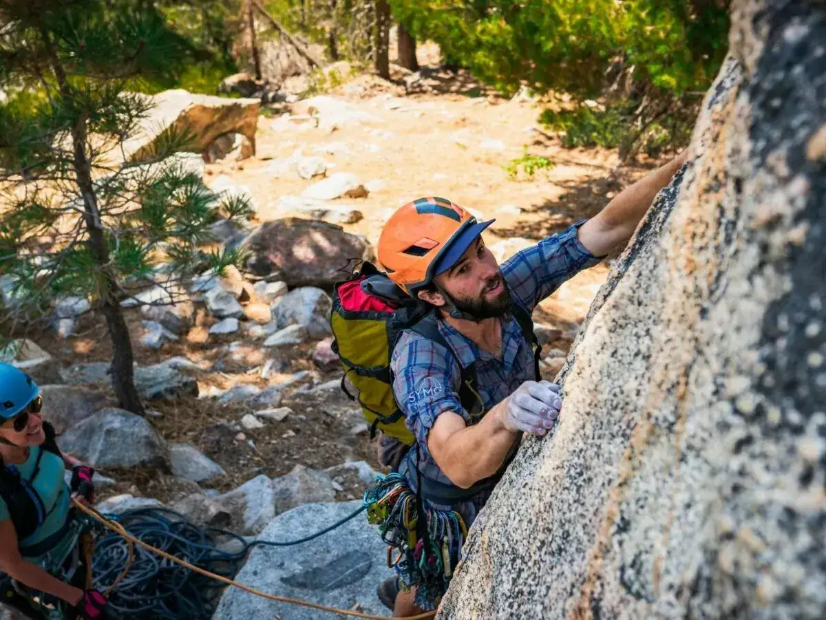 Mężczyzna w kasku wspina się po skale, a kobieta z linami czeka poniżej. Różne rodzaje wspinaczki wymagają różnego sprzętu i umiejętności.