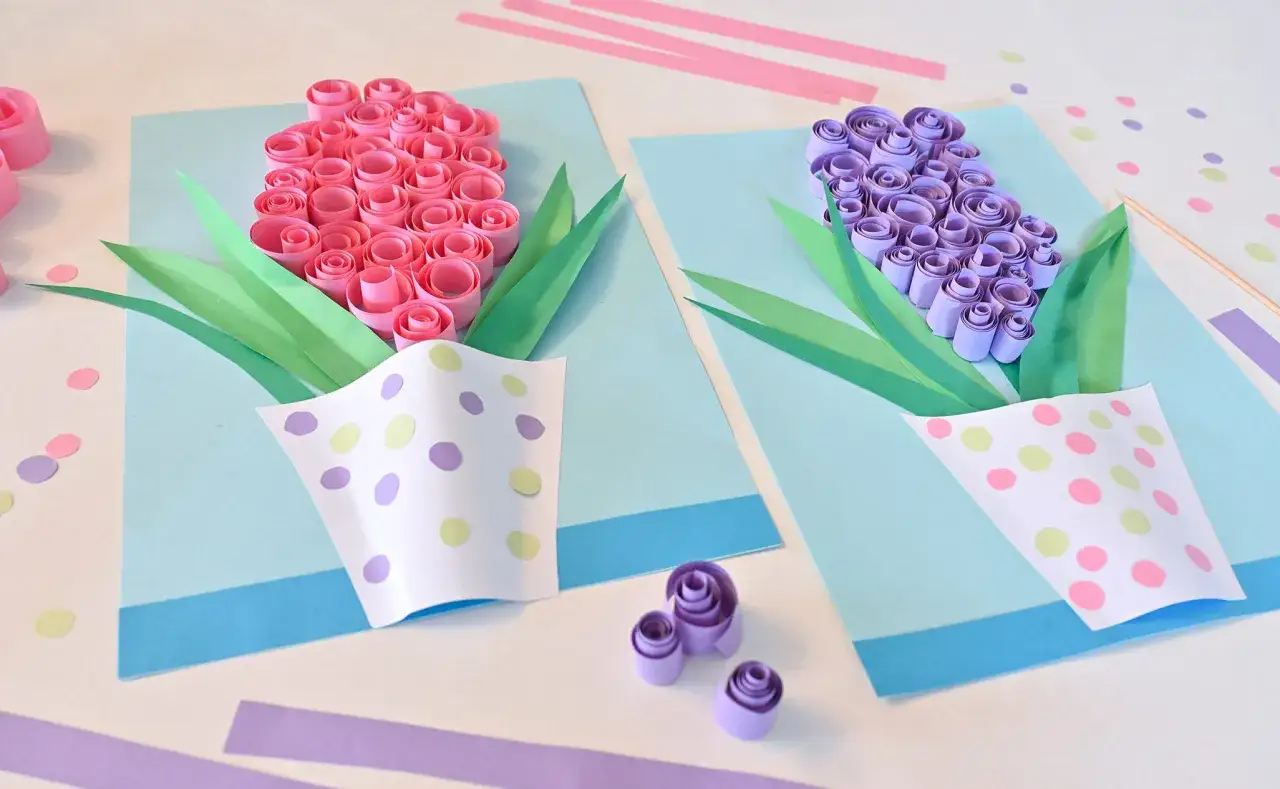 Urocza praca plastyczna wiosenna z papierowych kwiatów w doniczkach. Różowe i fioletowe kwiaty z rolkowanej bibuły, zielone liście i ozdobne doniczki w kropki.