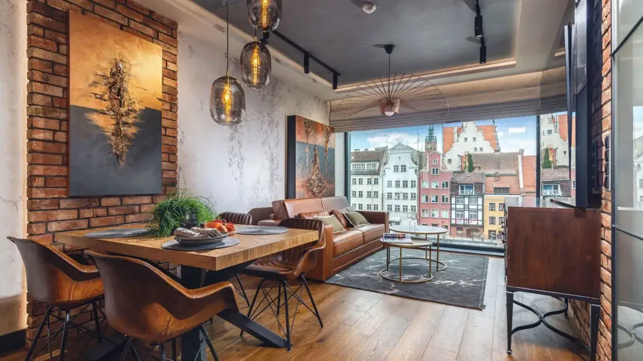 Nowoczesne oświetlenie salonu z jadalnią aranżacje: wiszące lampy nad drewnianym stołem i skórzaną kanapą, z widokiem na kolorowe kamienice.