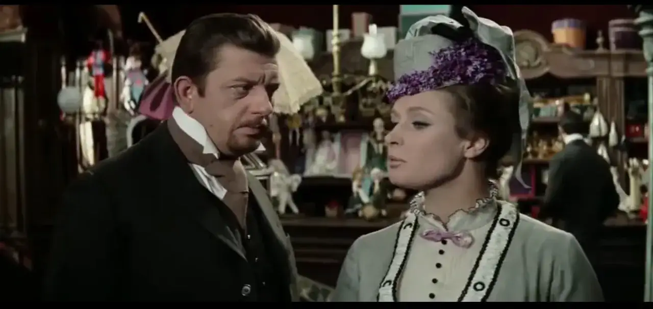 Mariusz Dmochowski w filmach, u boku pięknej kobiety w stylowym kapeluszu, w sklepie pełnym lalek i akcesori&oacute;w.