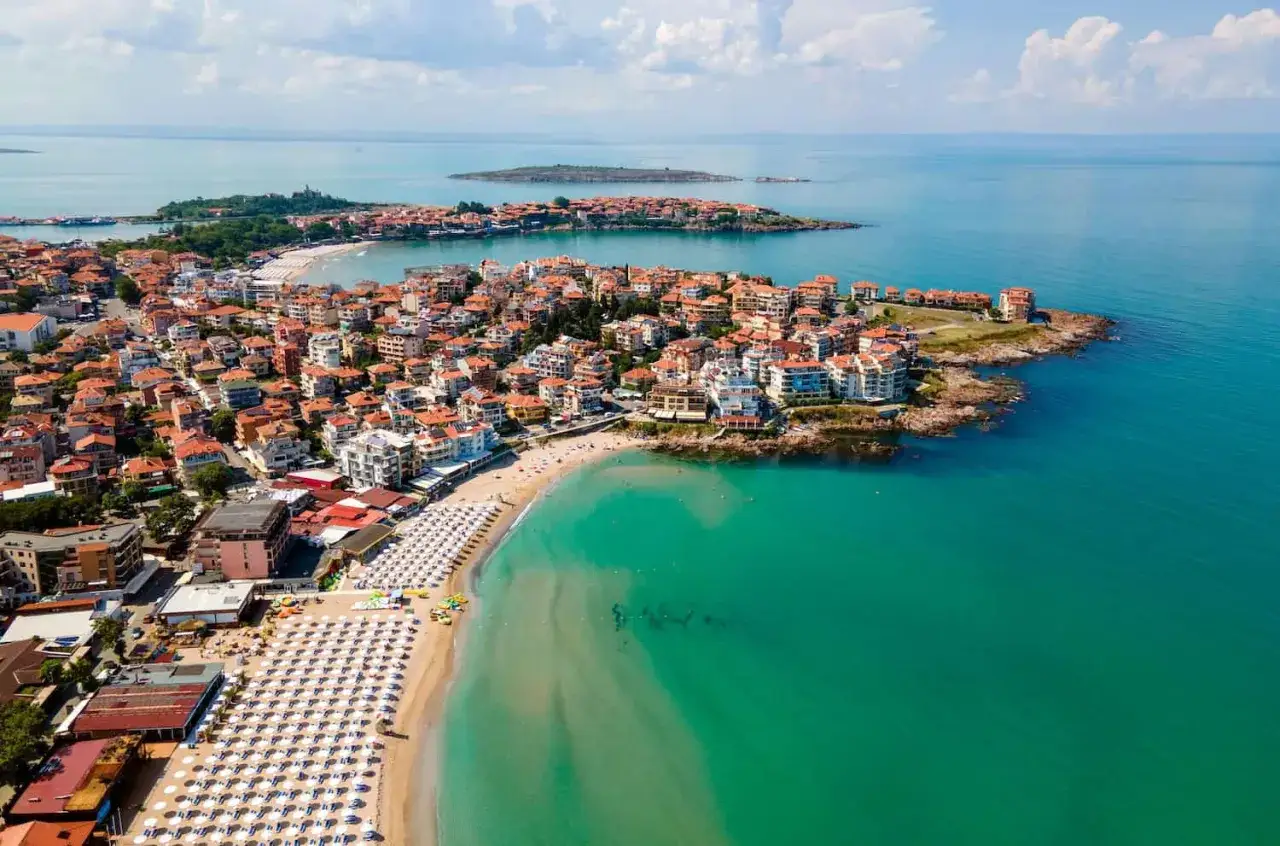 Widok z lotu ptaka na miasto z czerwonymi dachami i plażą z białymi parasolami, gdzie jest Burgas.