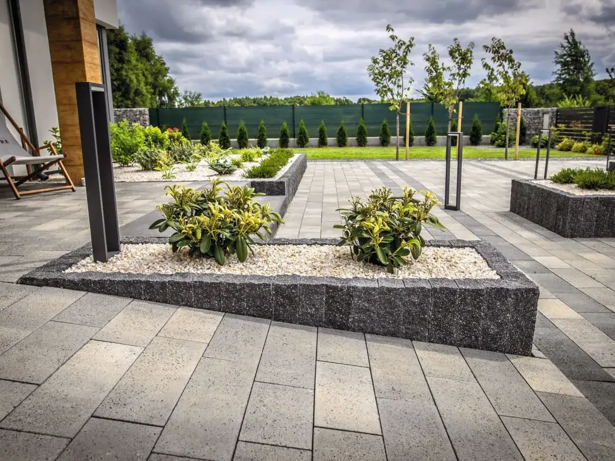 Nowoczesne kostka brukowa wokół domu tworzy elegancką przestrzeń z rabatami i roślinnością.