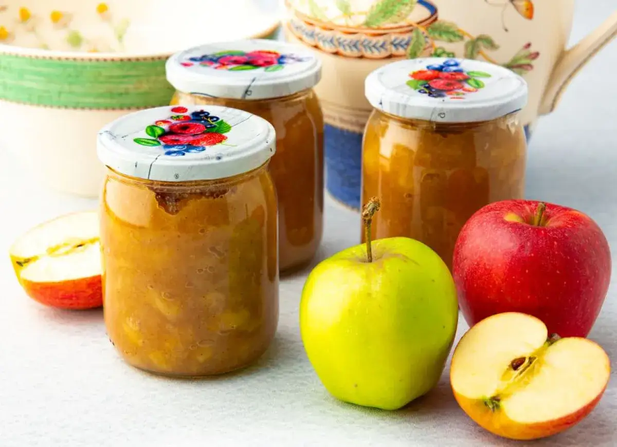 Słoiki z domowym musem jabłkowym, obok świeże jabłka. Idealny przepis na przetwory.