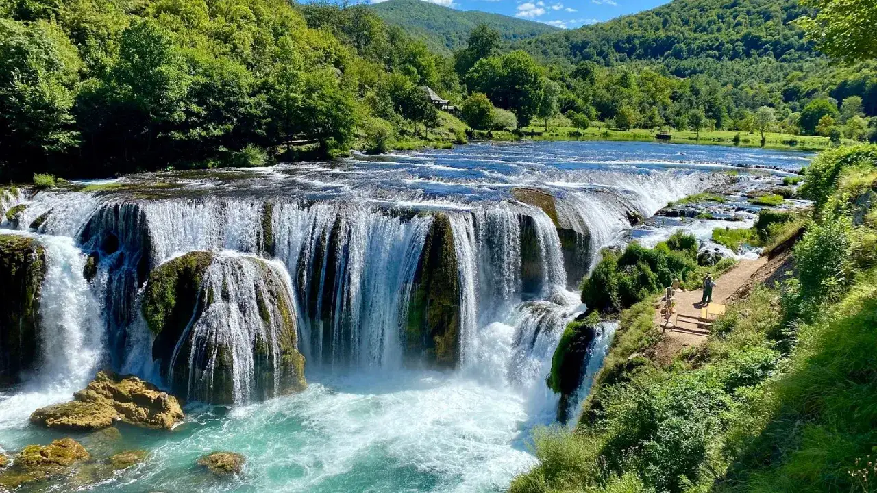 Potężne wodospady na rzece Una w otoczeniu bujnej zieleni. Woda spływa kaskadami po skałach, tworząc pianę.