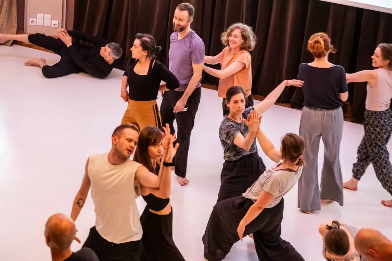 Choreograf kieruje grupą tancerzy podczas pr&oacute;by. Widać ruch, ekspresję i wsp&oacute;łpracę, co pokazuje, czym zajmuje się choreograf.