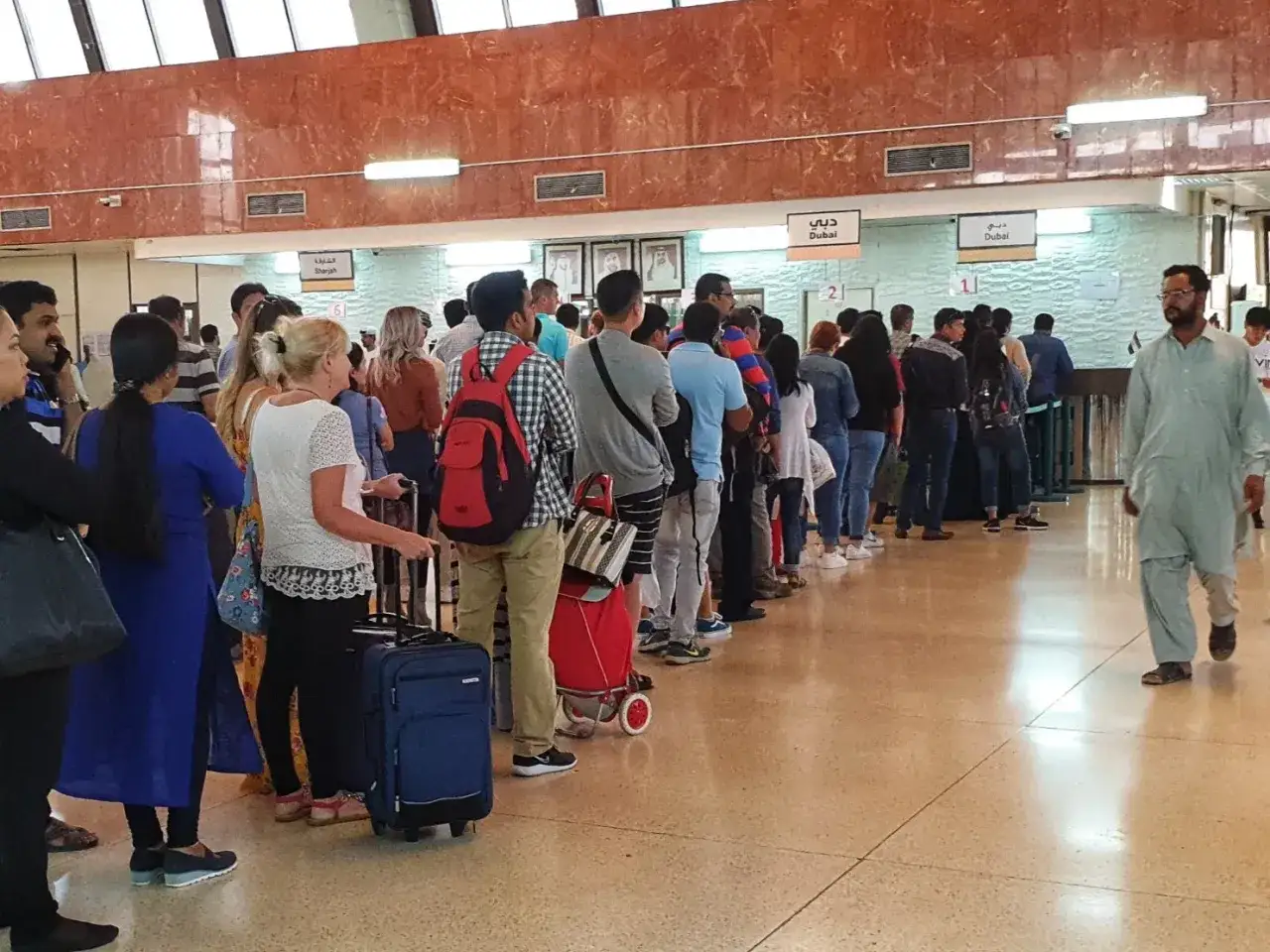 Długa kolejka ludzi z bagażami na lotnisku w Abu Zabi, czekających na odprawę.