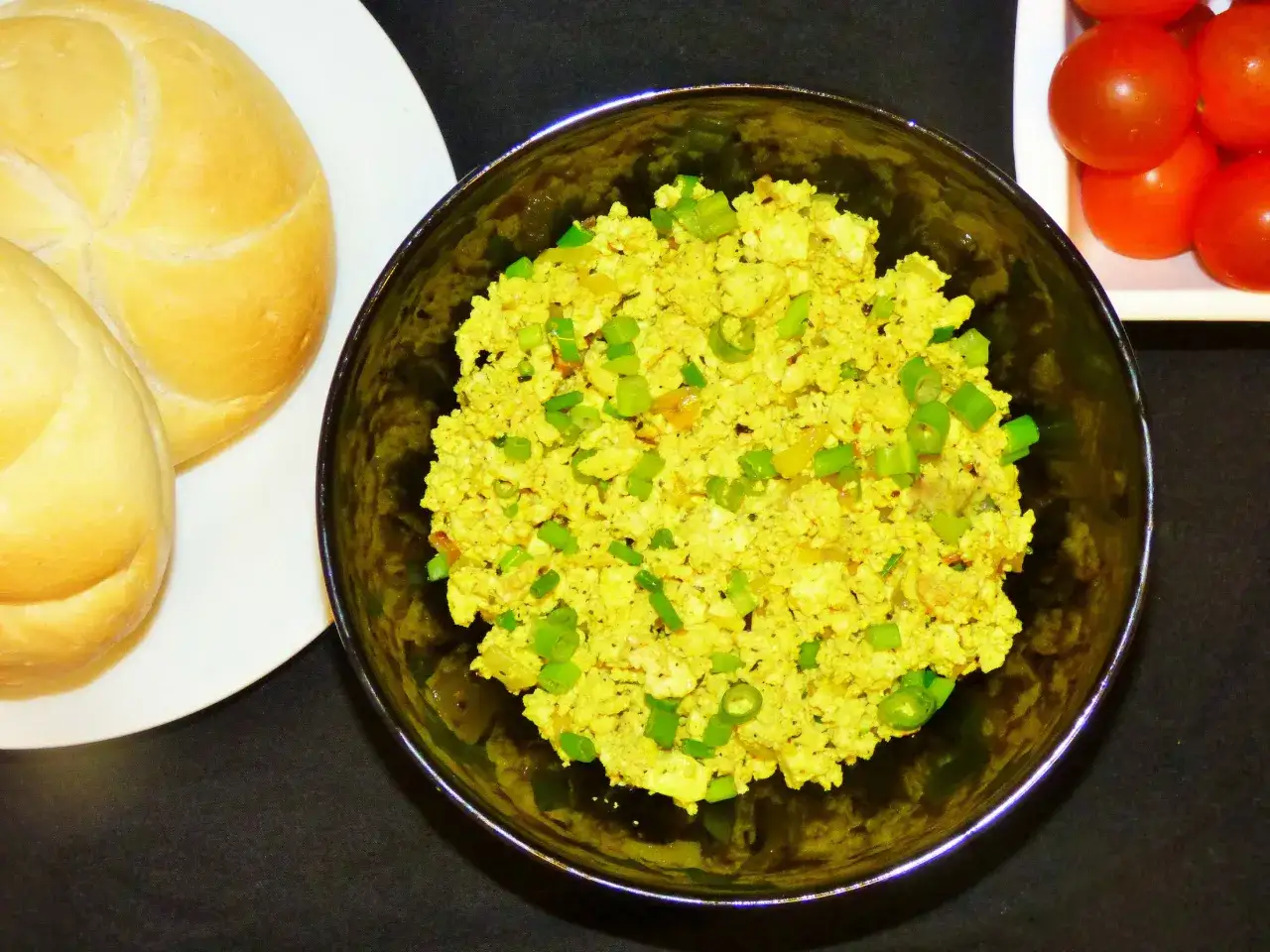 Jajecznica z tofu, zielona cebulka, bułki i pomidorki. Świetny spos&oacute;b, czym zastąpić jajka w diecie wegańskiej.