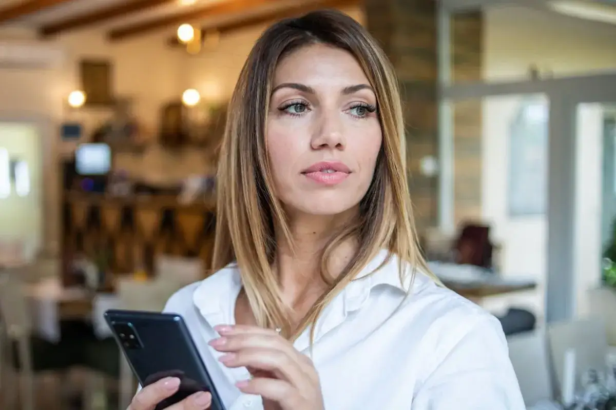 Zamyślona dziewczyna z telefonem w dłoni, jak pisze zakochana, z nadzieją w oczach.