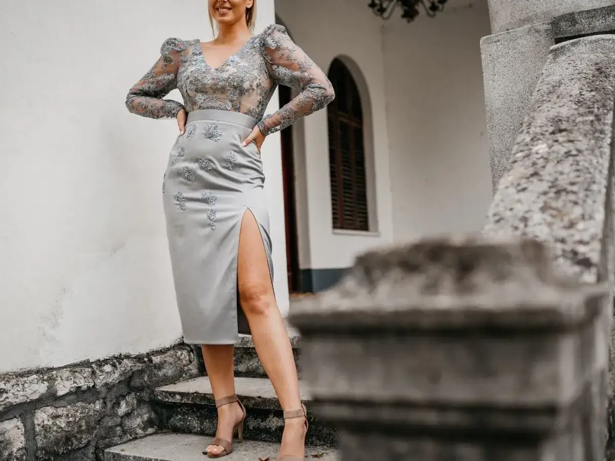 Elegancka szara sukienka z rozcięciem i koronkową górą, zestawiona z beżowymi sandałkami na obcasie. Idealne buty do szarej sukienki na specjalne okazje.