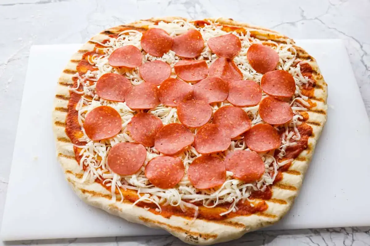 Pyszna pizza z grilla z serem i pepperoni, gotowa do pieczenia.