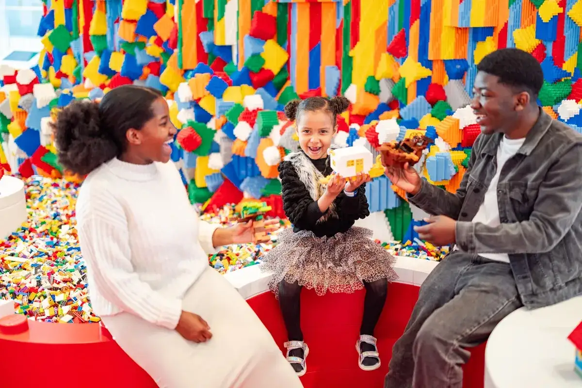 Rodzina bawi się klockami w kolorowym świecie Lego House w Billund. Dziecko trzyma biały domek.