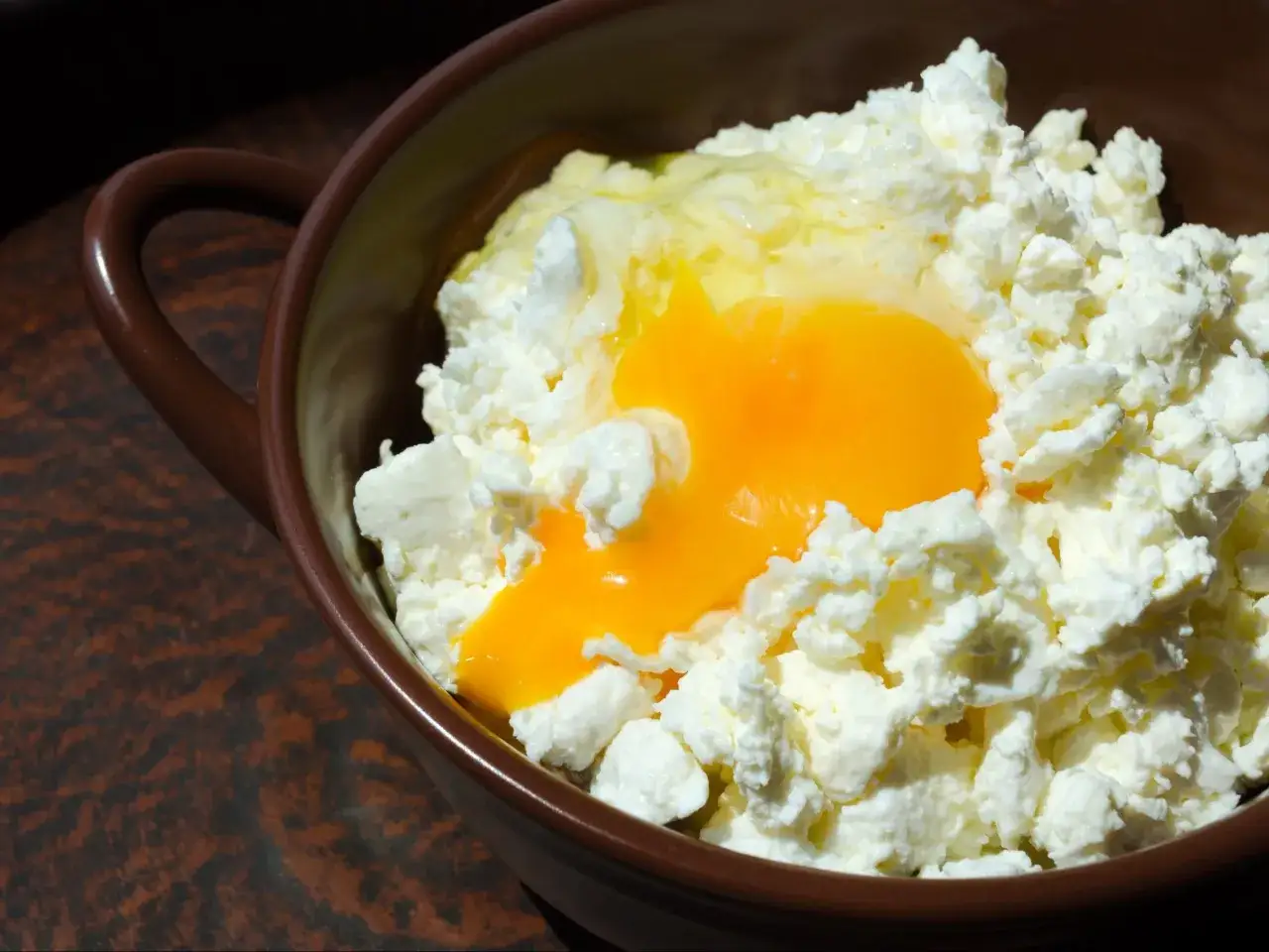 Twaróg z jajkiem w brązowej miseczce. Prosty pomysł na to, co można zrobić z twarogu na obiad.