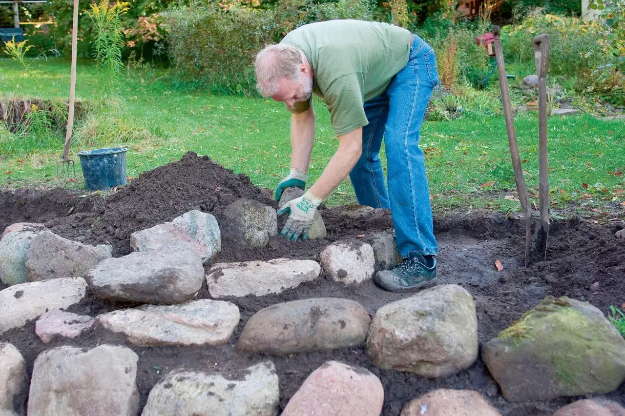 Mężczyzna układa kamienie polne, tworząc rabatę. Oto pomysły, co zrobić z kamieni polnych.