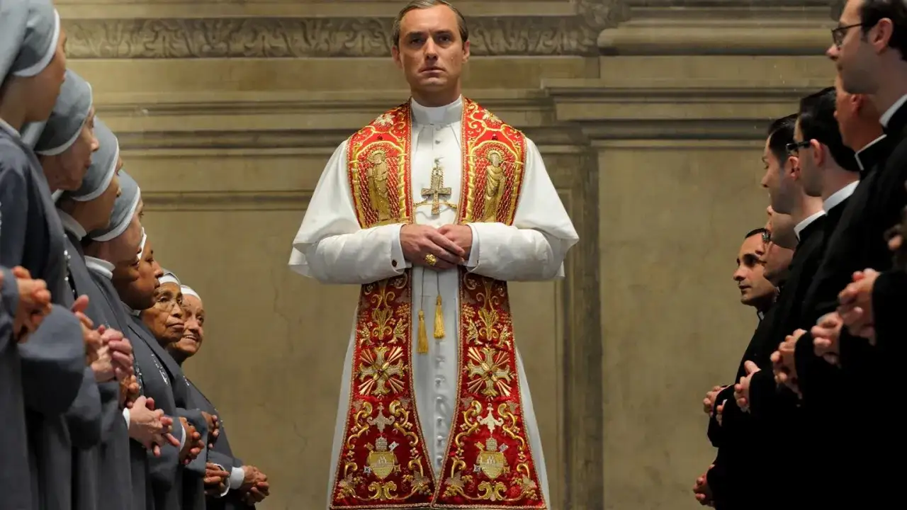 Jude Law jako młody papież Lenny Belardo w bogato zdobionej szacie, otoczony przez siostry zakonne i księży.