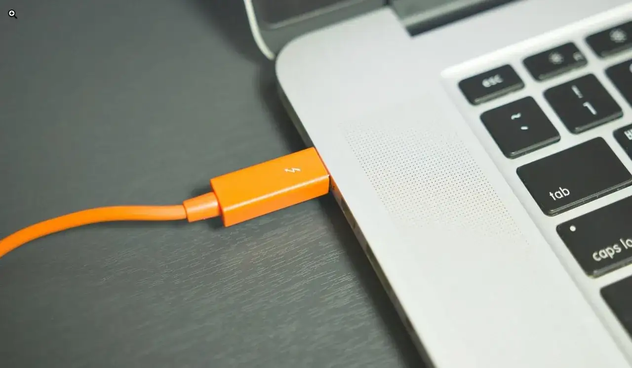 Pomarańczowy kabel z wtyczką Thunderbolt podłączony do MacBooka. Dowiedz się, jak otworzyć pendrive na macbooku.
