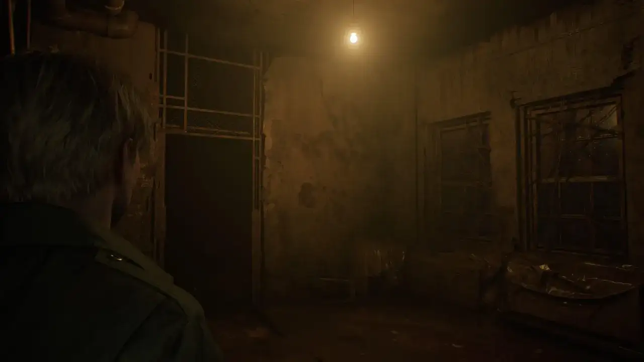 Mroczny korytarz w Silent Hill remake. James Sunderland stoi przed kratami, a nad nim wisi żarówka.