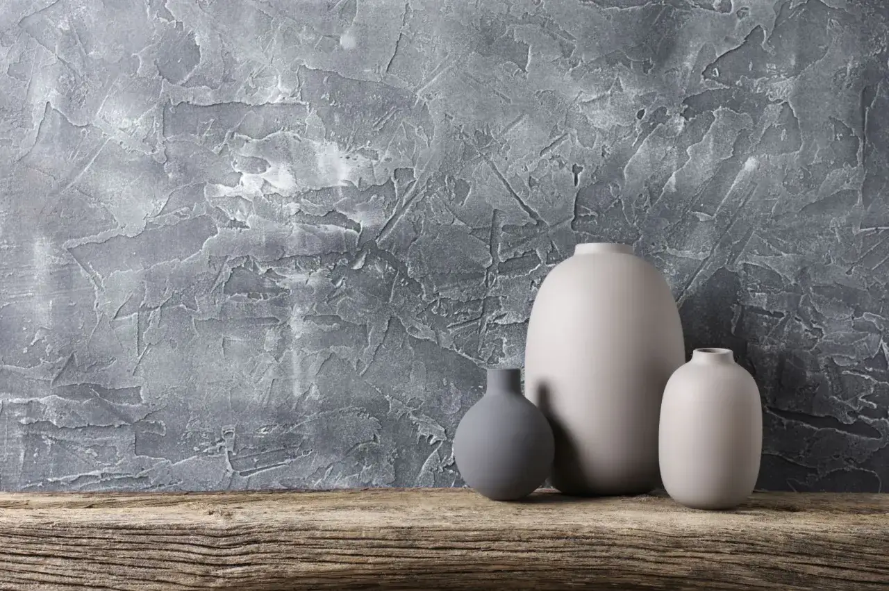 Szare wazony na drewnianej półce pod tynkiem strukturalnym. Zastanawiasz się, ile kosztuje położenie tynku strukturalnego?