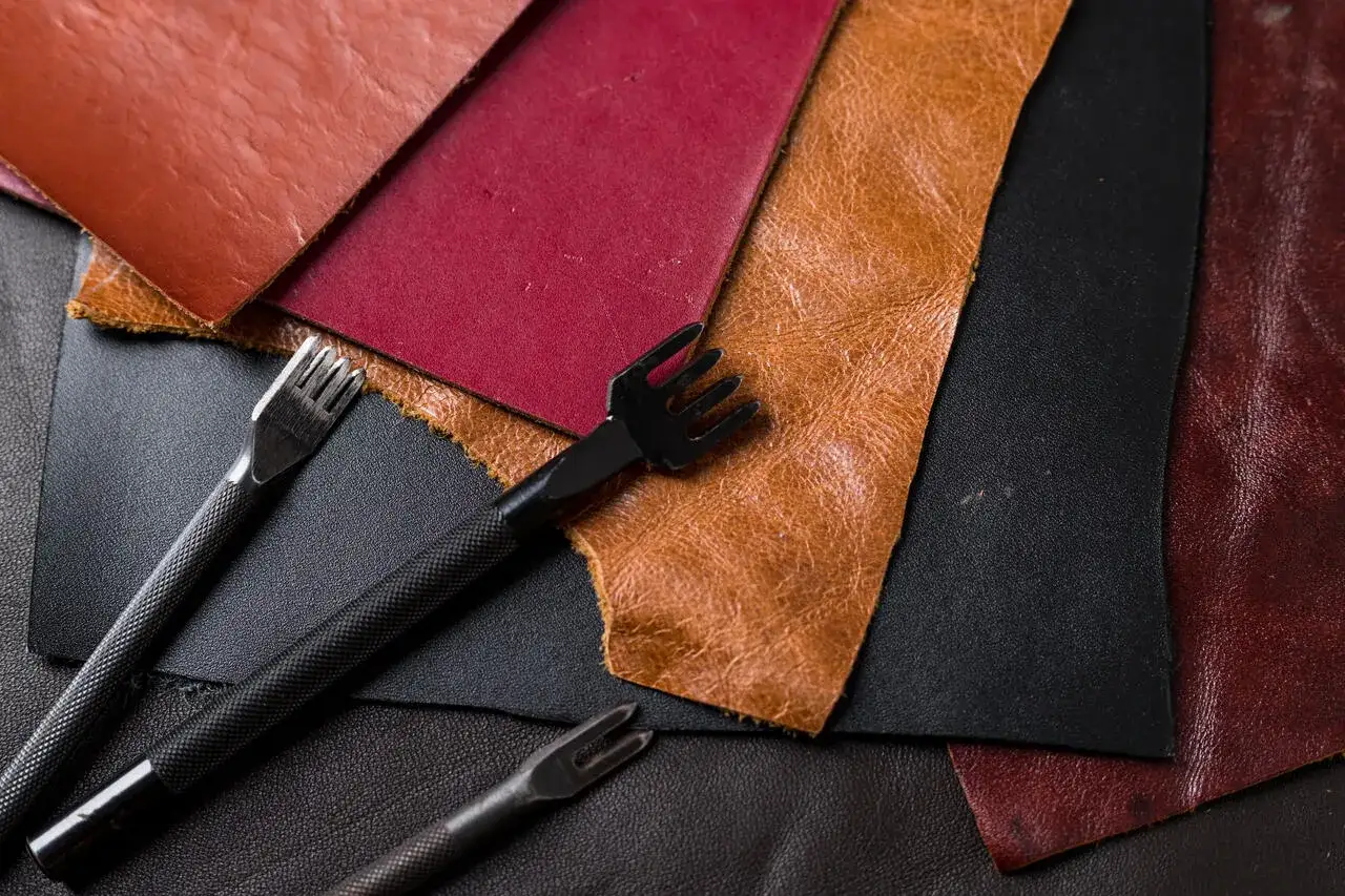 R&oacute;żne rodzaje sk&oacute;ry naturalnej: brązowa, bordowa, czarna i rudawa, obok narzędzi do jej obr&oacute;bki.