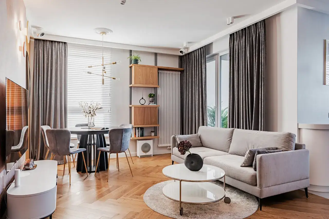 Szare zasłony idealnie komponują się z jasną kanapą, tworząc spójną aranżację salonu.