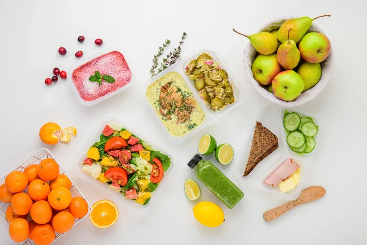 Catering dietetyczny co to? Zestawy posiłków w pojemnikach: sałatka, ryba z sosem, kanapka, owoce, warzywa i zielony koktajl.