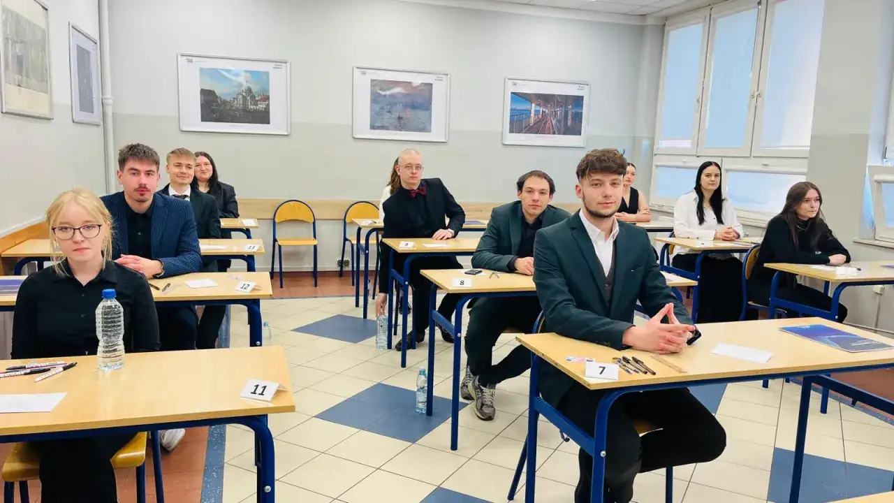 Uczniowie w garniturach i eleganckich strojach siedzą przy ławkach, gotowi do egzaminu. Czy w technikum jest matura? Tak, to właśnie ten dzień!
