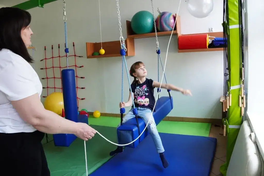 dziecko bawi się masami sensorycznymi, dziecko na huśtawce terapeutycznej, dziecko na trampolinie