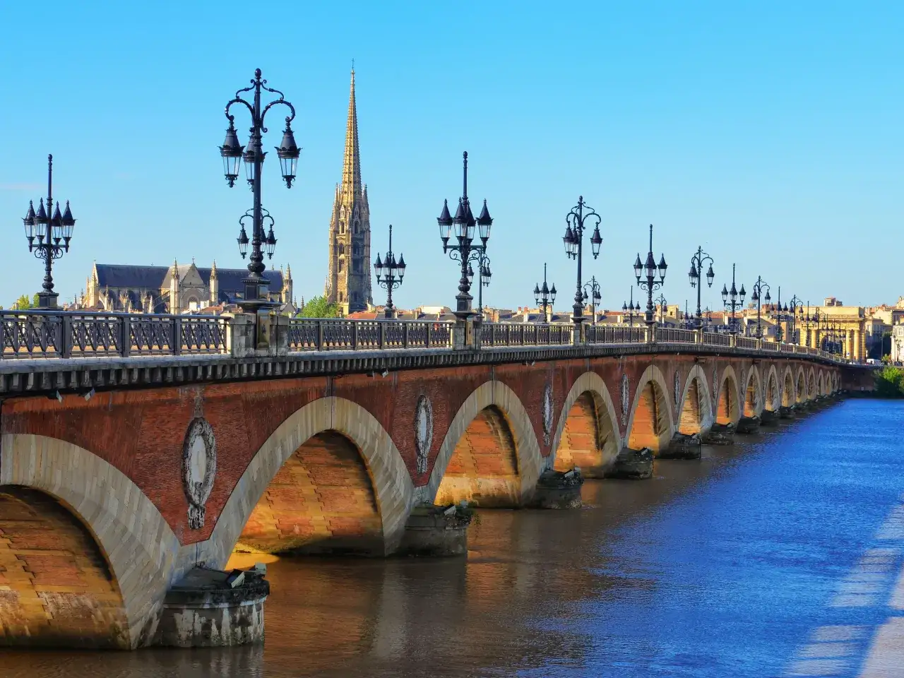 Most Pont de Pierre w Bordeaux, z zabytkowymi latarniami i katedrą w tle. Planujesz podróż? Sprawdź, ile euro na tydzień do Francji potrzebujesz!
