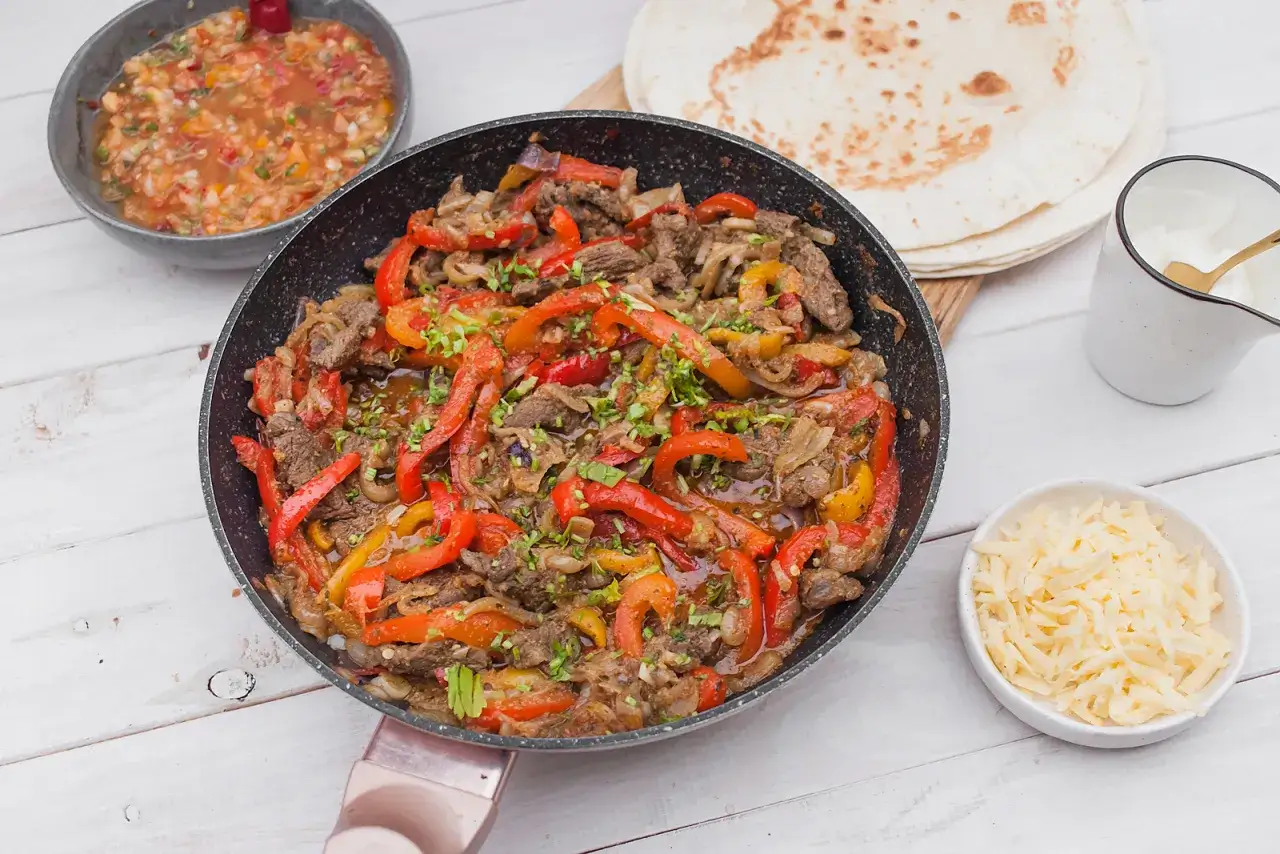 Fajitas co to? Aromatyczne mięso z papryką i cebulą na patelni, podane z tortillami, salsą i serem.