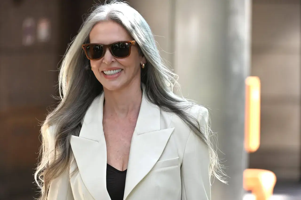 Elegancka kobieta w okularach i białej marynarce, z długimi, siwymi włosami. Inspiracja, jak nosić siwe włosy z klasą.