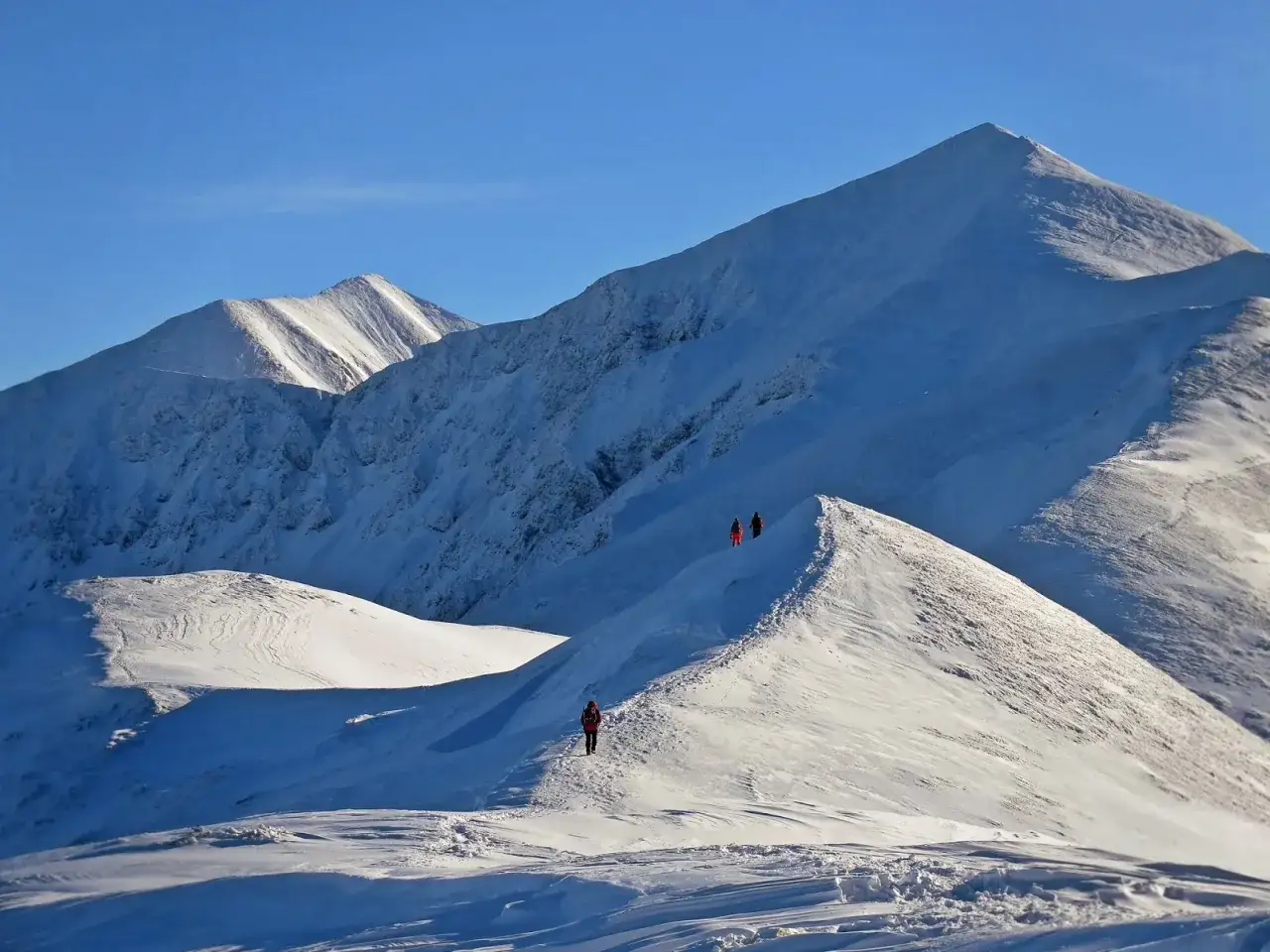 Zimowe Tatry: turyści przemierzają ośnieżone grzbiety. To idealne miejsce na łatwe szlaki w Tatrach zimą, gdzie można podziwiać piękne widoki.