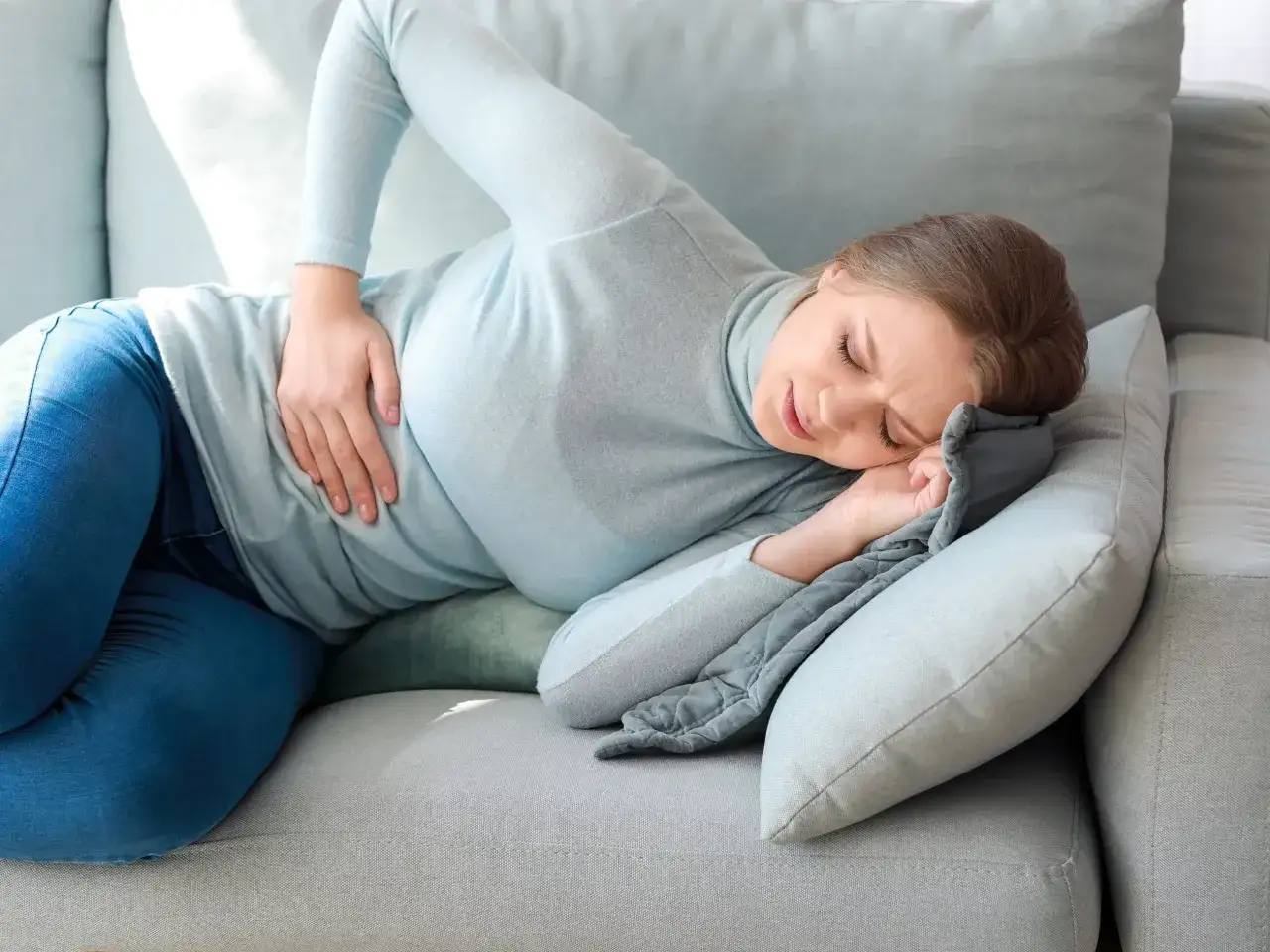 Kobieta cierpi na ból brzucha, szukając ulgi w domowych sposobach.