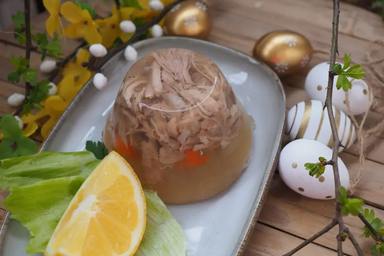 Galareta wieprzowa z marchewką, podana z cytryną i sałatą. Obok wielkanocne jajka i wiosenne kwiaty.