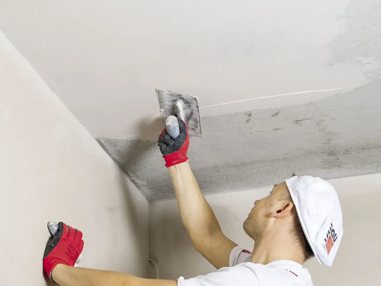 Malarz w rękawicach nakłada gładź na sufit, pokazując, jak wygładzić ściany.
