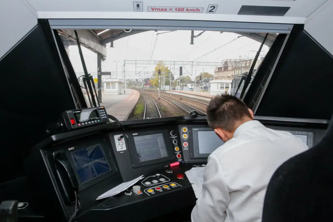 Motorniczy pociągu w kabinie, przed nim pulpit sterowniczy i tory. Ciekawe, ile zarabia motorniczy pociągu?