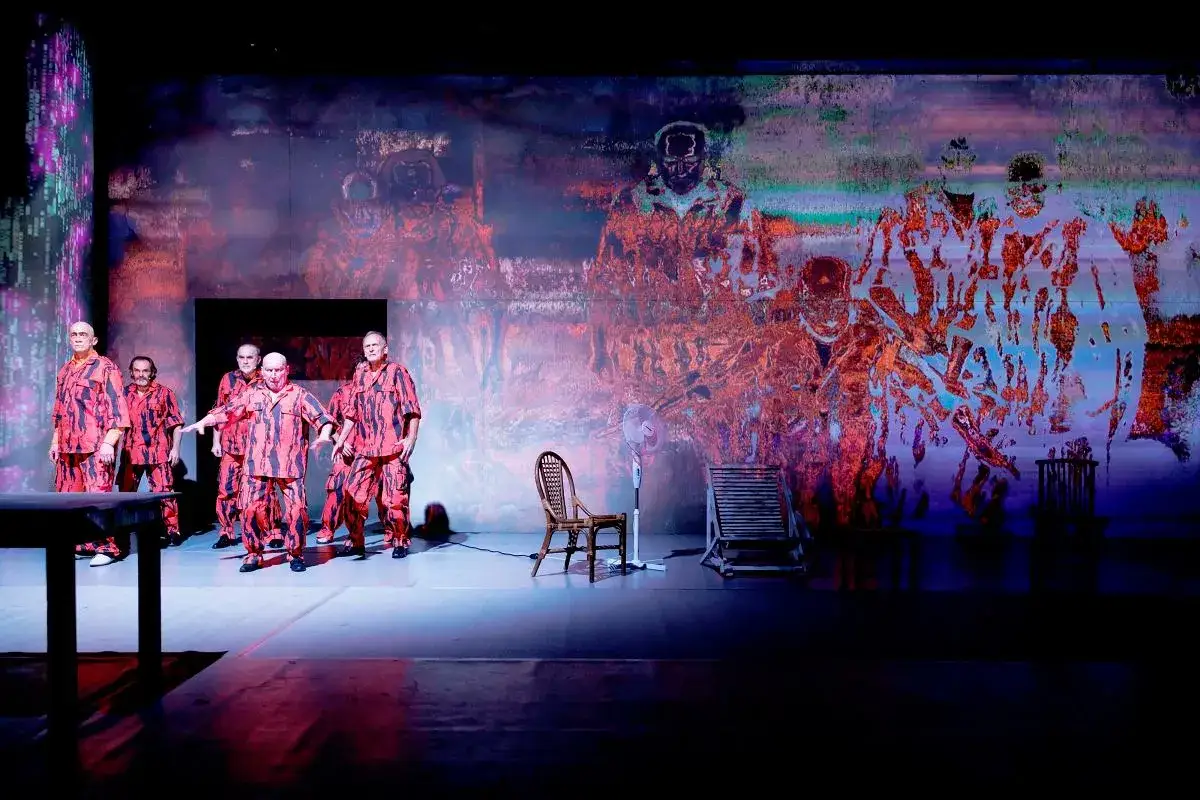 Aktorzy w czerwono-czarnych strojach na scenie. Jan Klata reżyseruje teatr pełen surrealistycznych projekcji.