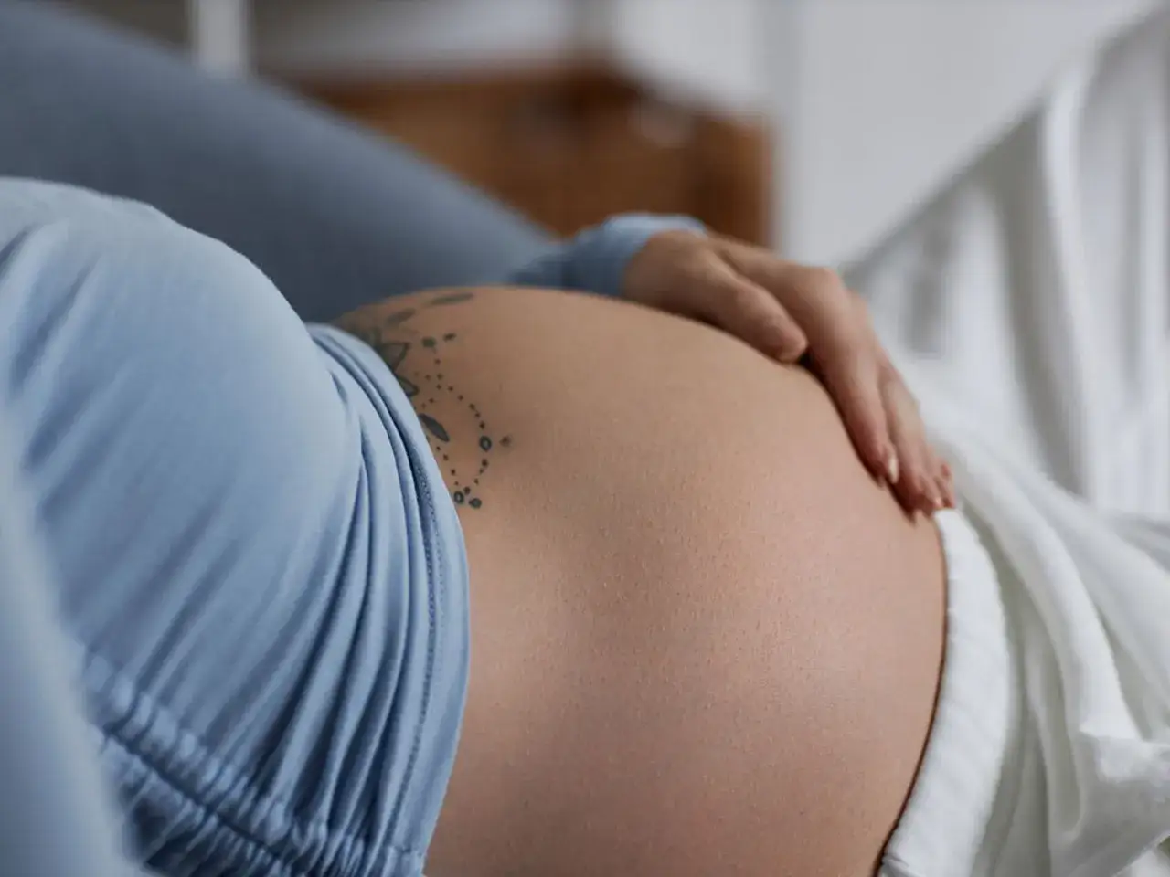 Dłoń na twardym brzuchu przed porodem. Delikatny tatuaż zdobi sk&oacute;rę.