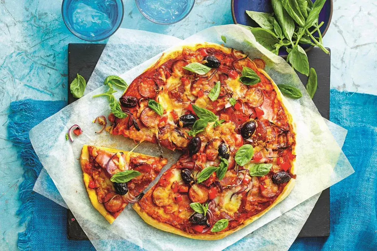 Pyszna pizza z gotowego ciasta, obficie posypana salami, oliwkami i bazylią. Idealna na szybki obiad.