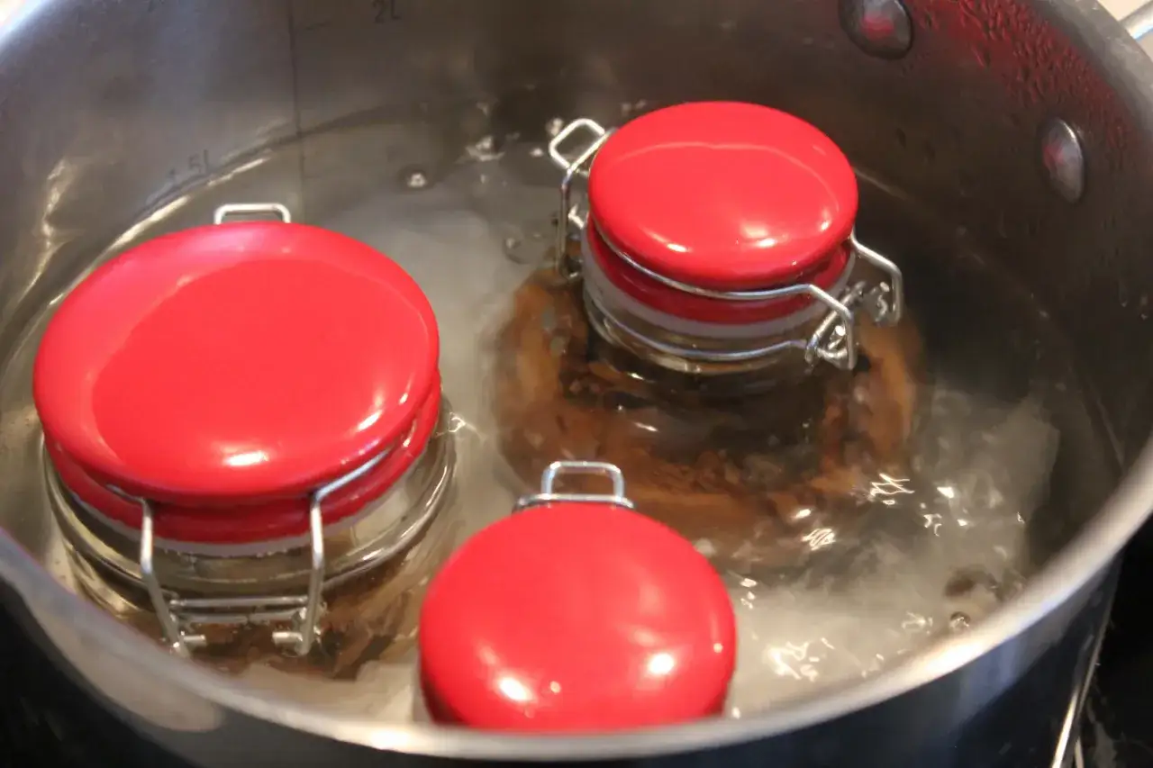 Słoiki z sosami do spaghetti gotują się w garnku. To kluczowy etap, jak zawekować sos do spaghetti, by cieszyć się nim dłużej.