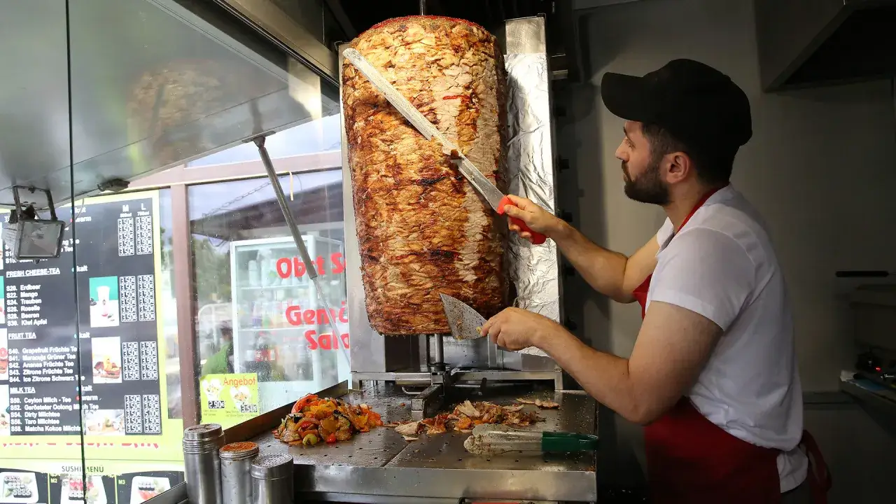 Sprzedawca kroi mięso na kebabie. Ceny w menu sugerują, że ile kosztuje kebab w Niemczech, to około 3,50-3,90 euro.