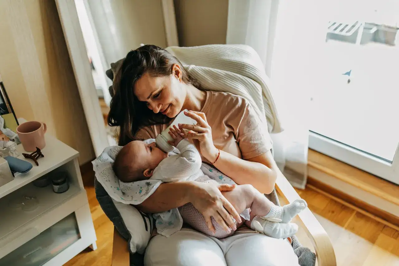 Uśmiechnięta mama karmi butelką niemowlę. Warto wiedzieć, co ile karmic 4 miesieczne niemowle, by zapewnić mu najlepszą opiekę.