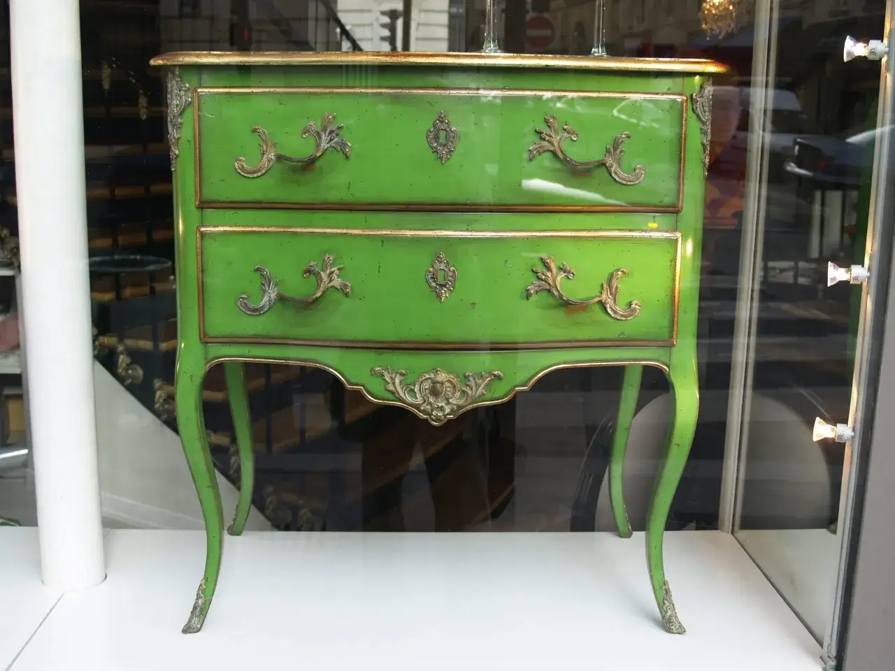 Zielona komoda z pozłacanymi zdobieniami, gotowa do renowacji antyków. Jej elegancki kształt i bogate detale zapowiadają odzyskanie dawnego blasku.