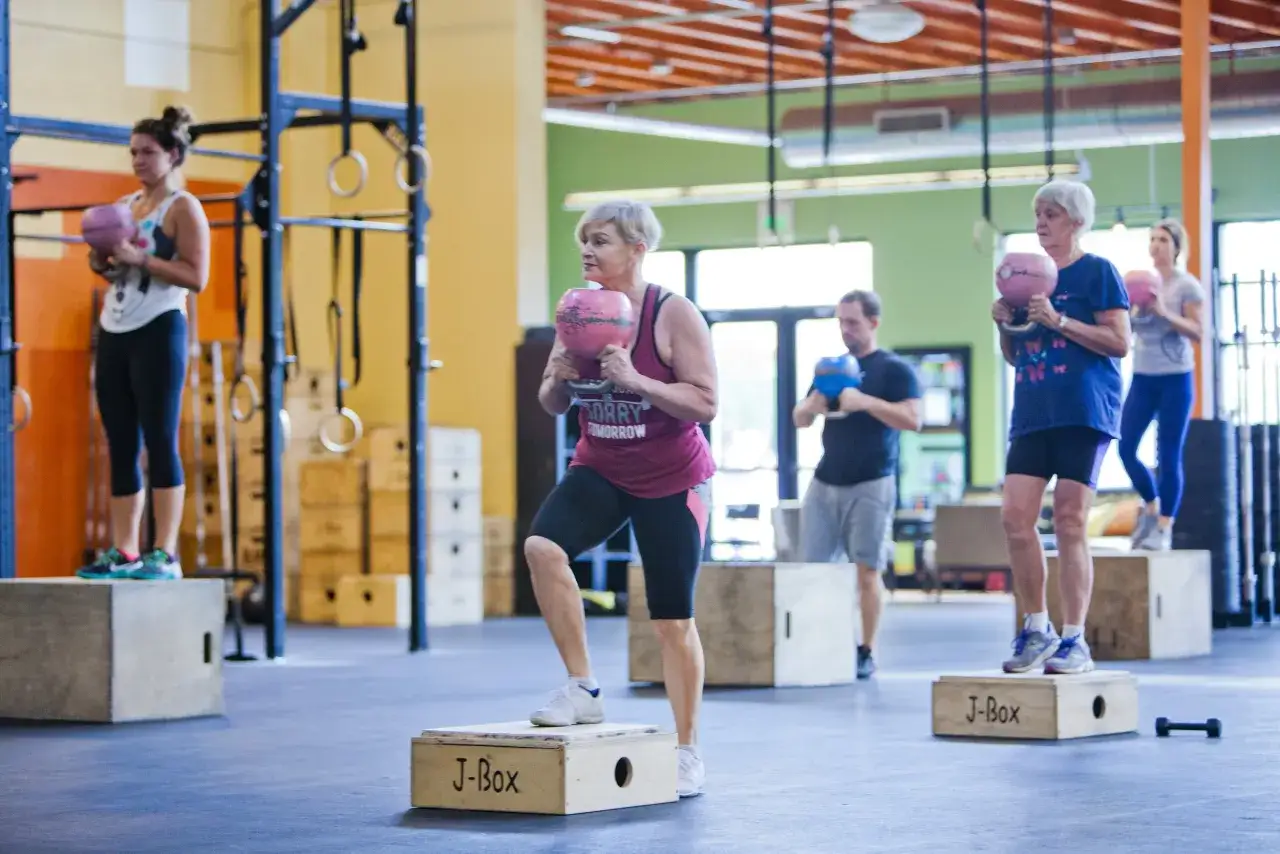 Grupa osób ćwiczy crossfit, wykonując ćwiczenia z kettlebellami na skrzyniach.