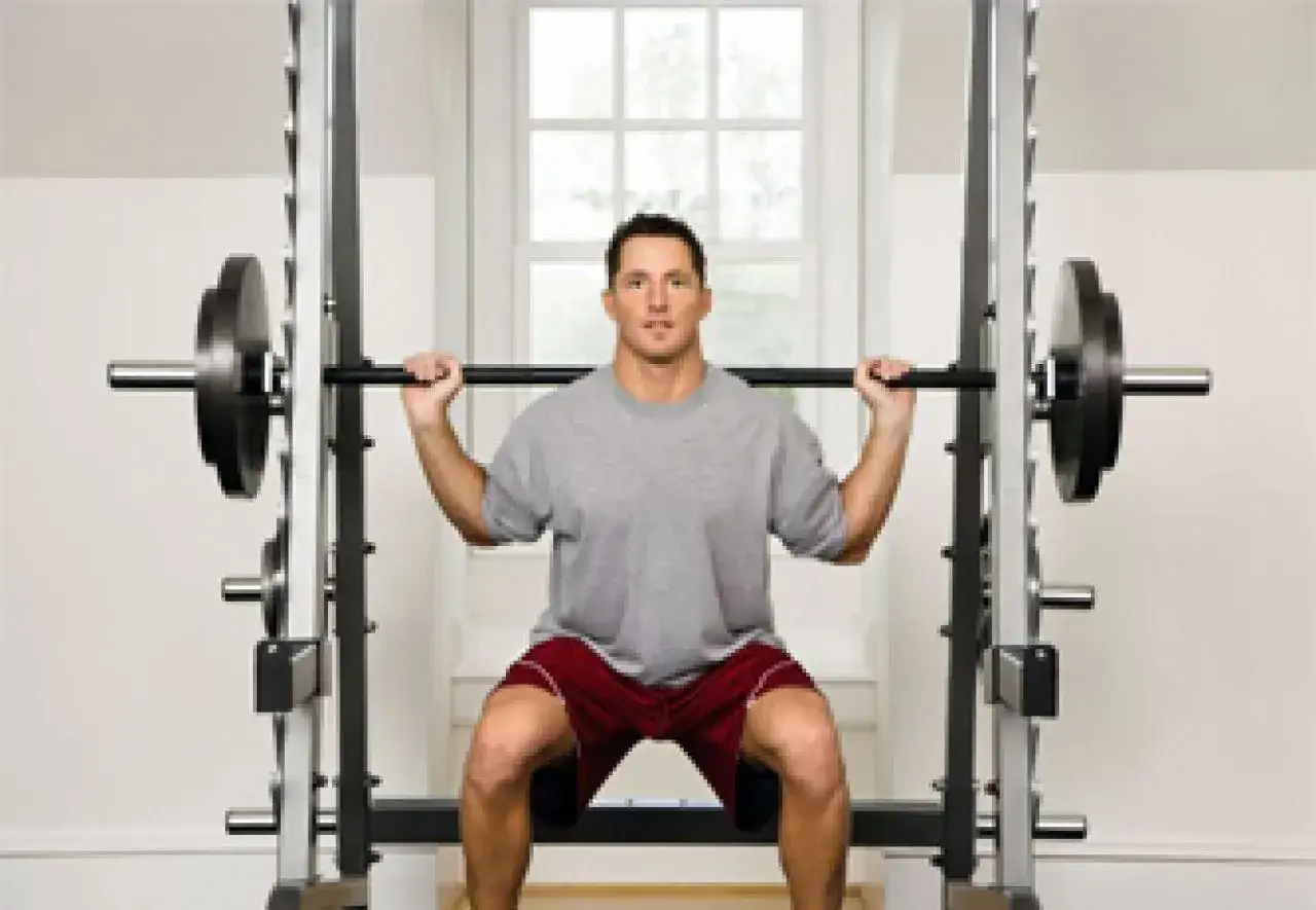 Mężczyzna wykonuje przysiady z obciążeniem na sztandze w klatce.