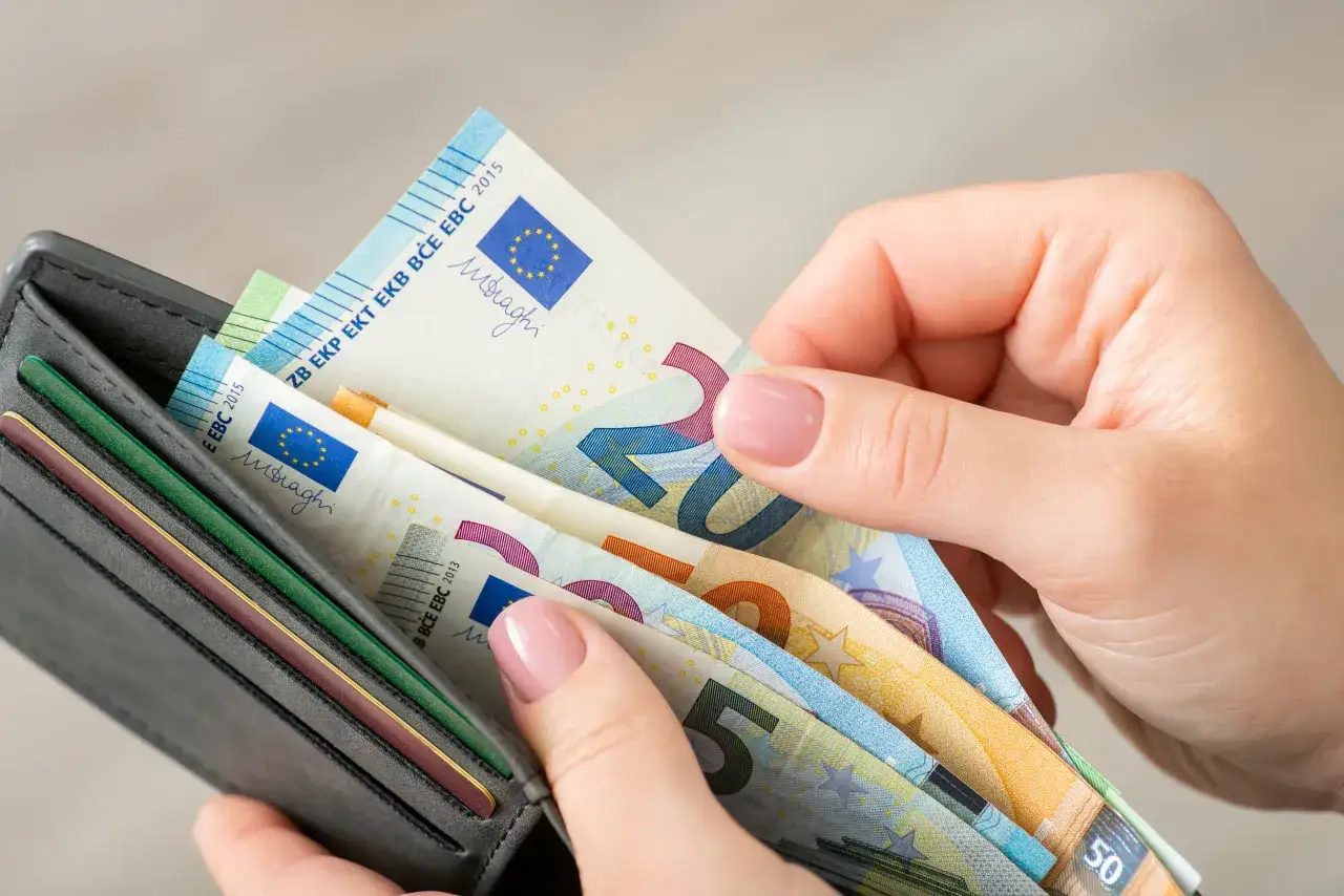 Dłonie trzymają portfel z banknotami euro. Zastanawiasz się, ile euro można przewieźć przez granicę na osobę?