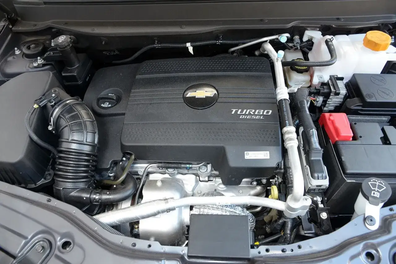 Silnik Turbo Diesel w Chevrolet Captiva. Widoczne elementy układu dolotowego i osłona silnika z logo.