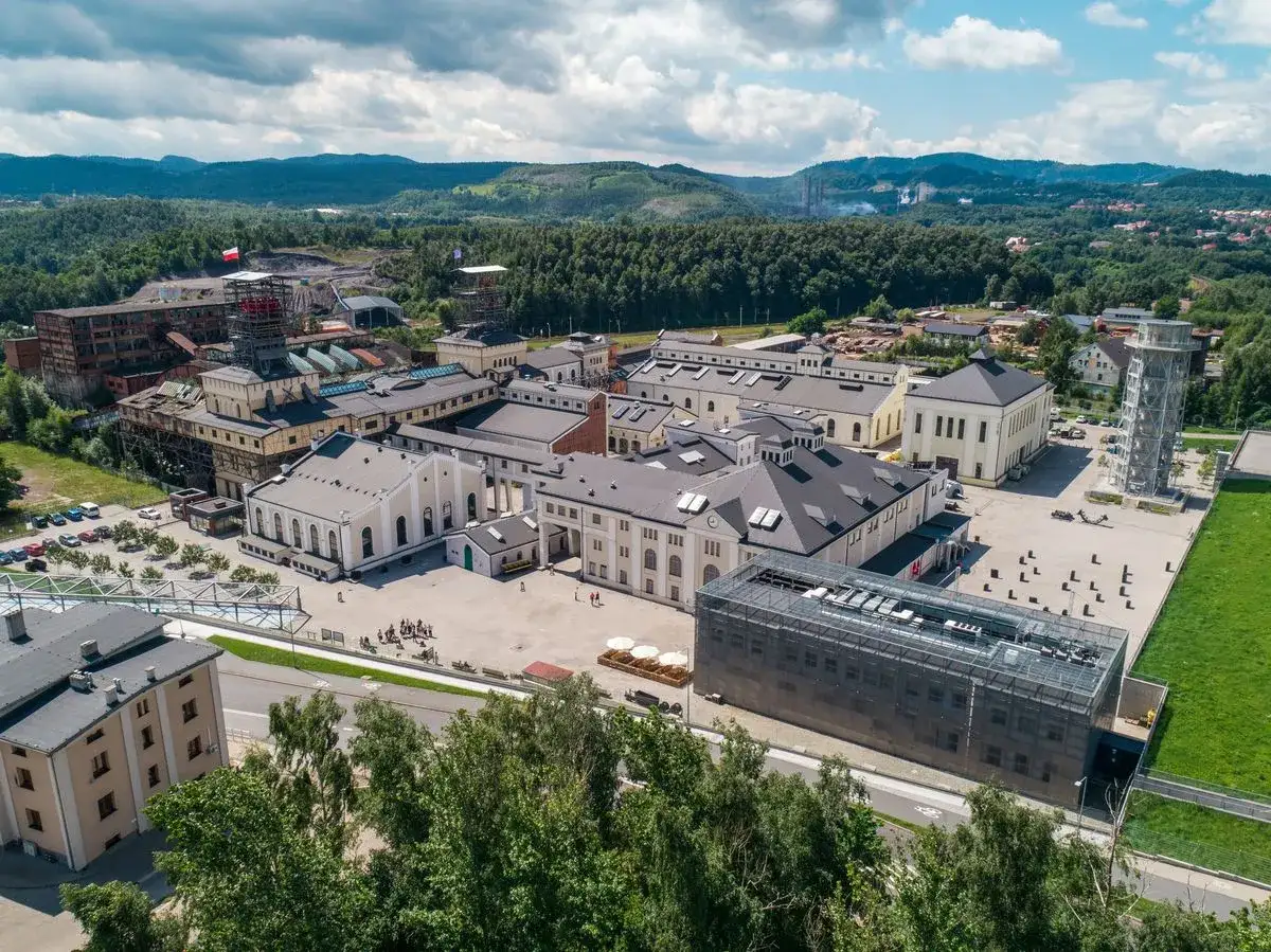 Wałbrzych atrakcje: kompleks przemysłowy z wieżą widokową i nowoczesnymi budynkami, otoczony zielenią i górami.