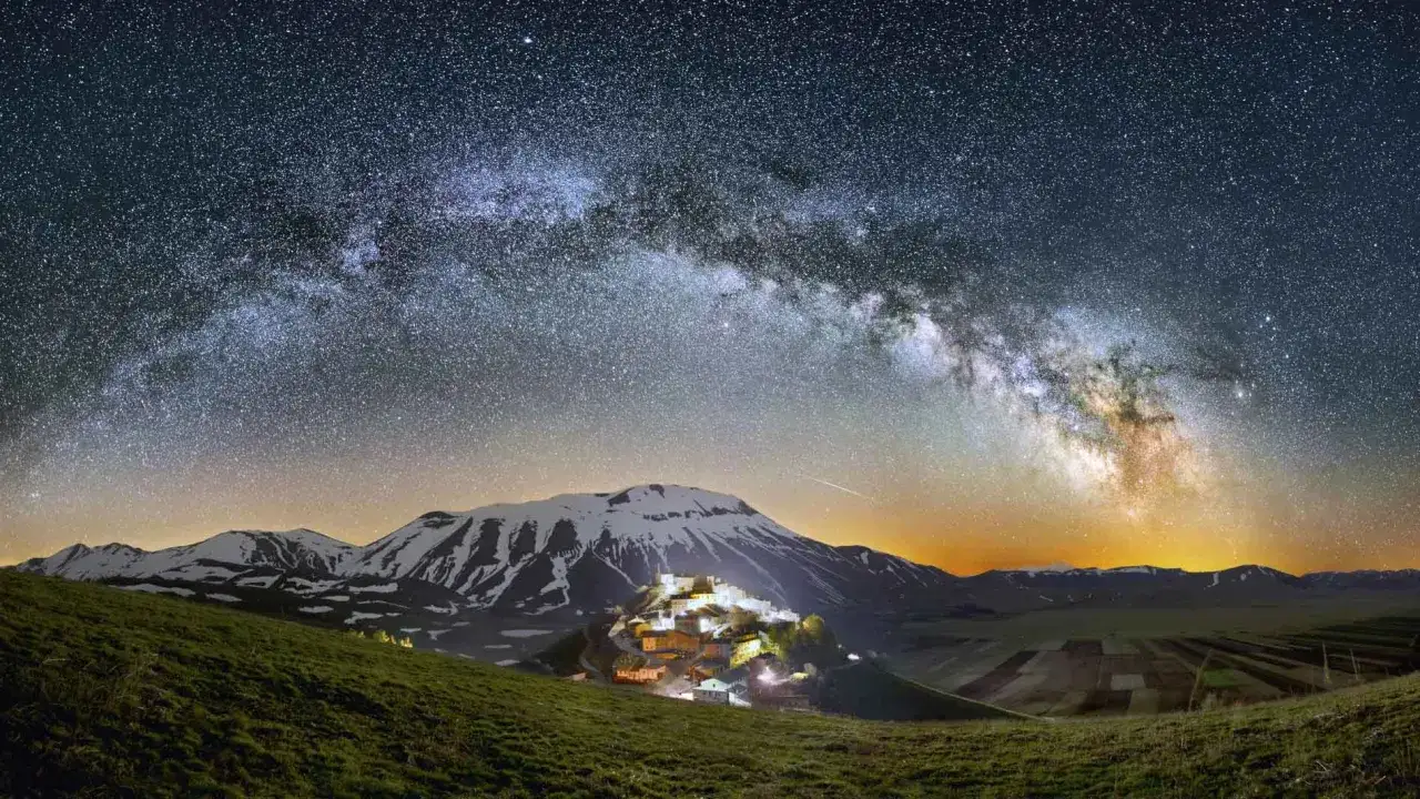 Niesamowita fotografia astronomiczna: Droga Mleczna nad ośnieżonymi górami i oświetloną wioską.