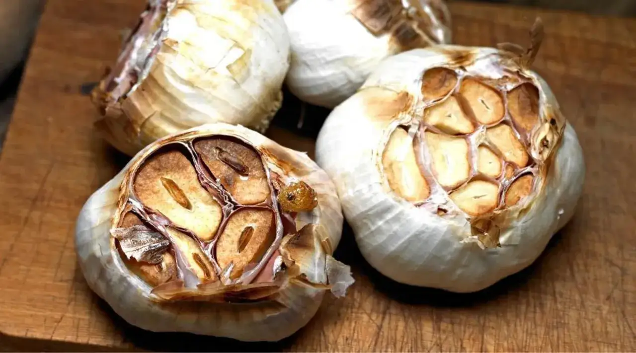 Aromatyczny czosnek z grilla, z lekko przypieczonymi ząbkami, gotowy do wyciśnięcia na deskę.