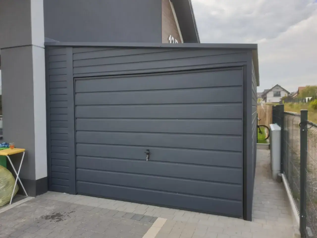 Nowoczesny garaż z dachem jednospadowym, szary, z segmentową bramą. Obok stoi rower.